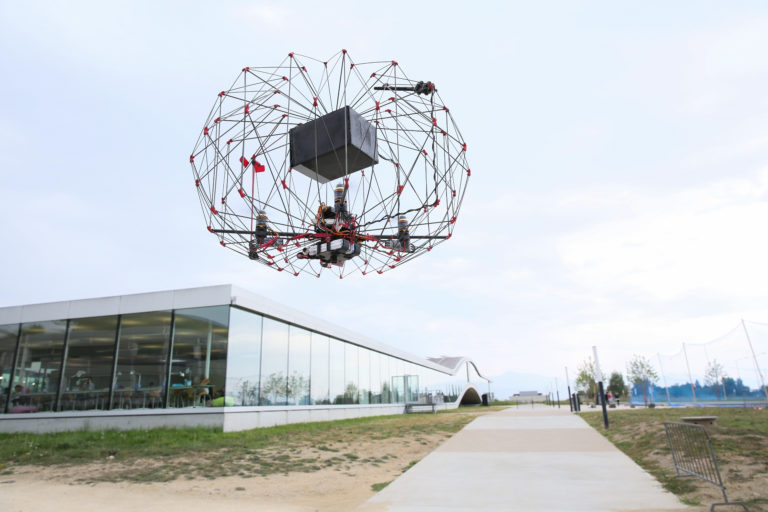 Picture of a flying drone with an exterior structure that protects it and a box inside that allows it to carry things