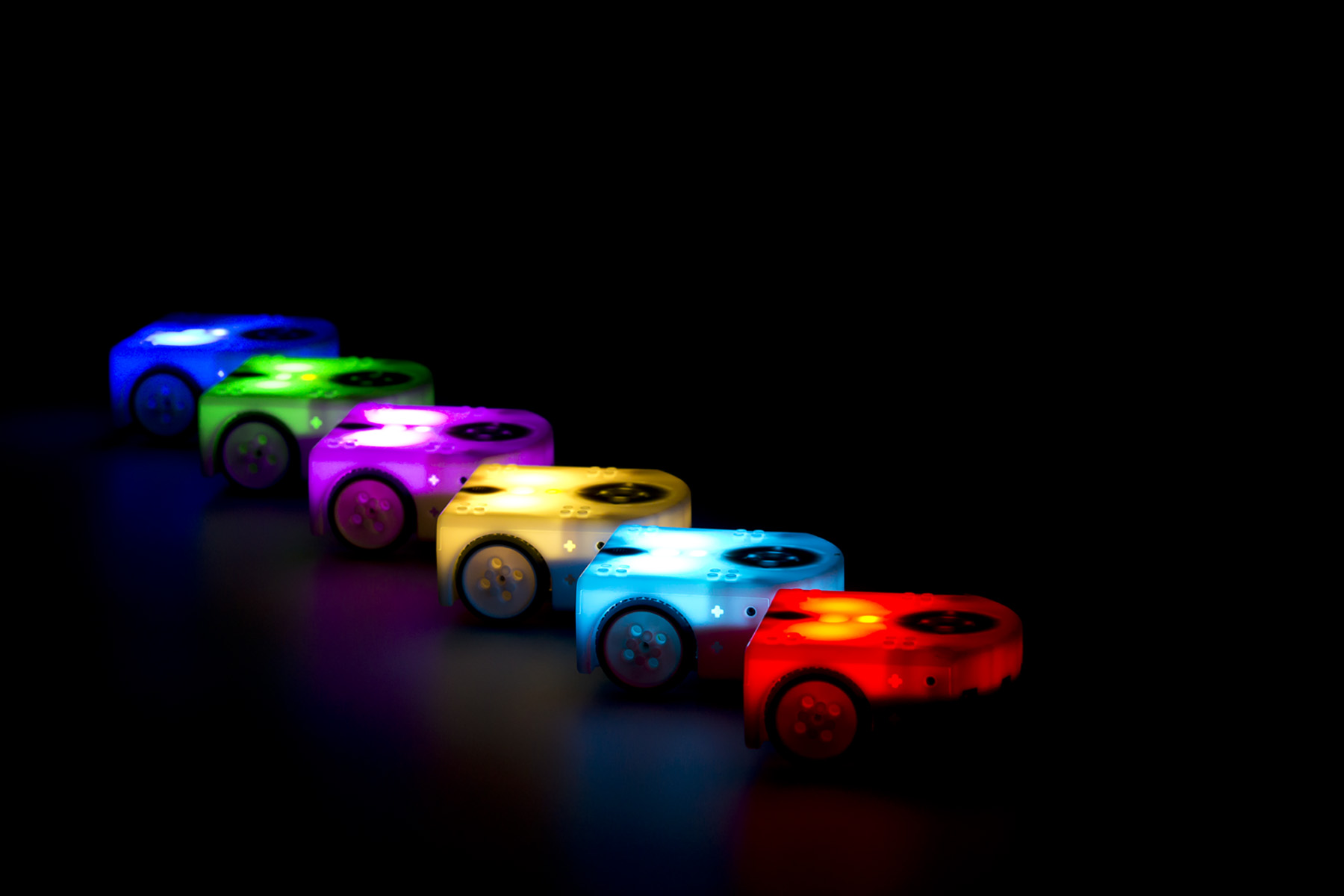 6 lighted Thymio robots in different colors in a dark background