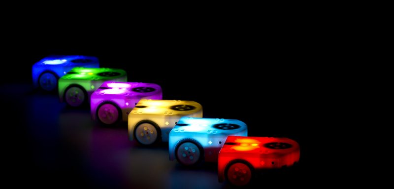 6 lighted Thymio robots in different colors in a dark background